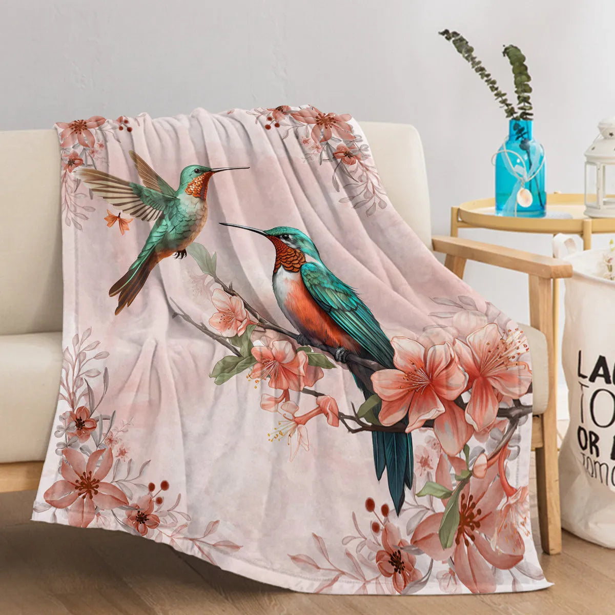 Hummingbird floral fleece throw blanket in pink flannel velvet, shown on sofa with hemmed edges