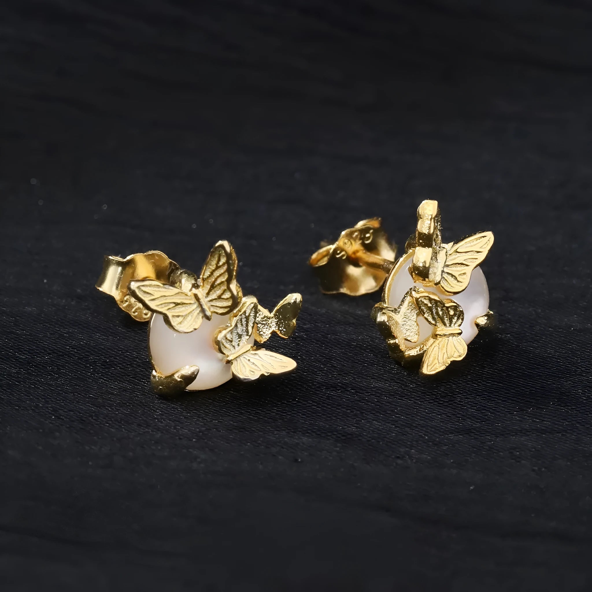 Close-up of a pair of silver butterfly stud earrings with a gold-toned finish.