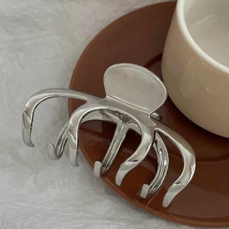Assorted silver metal hair claws and barrettes including wave, knot, bow, and pearl designs on a white background.