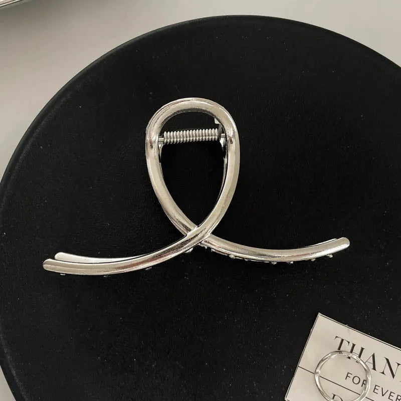 Assorted silver metal hair claws and barrettes including wave, knot, bow, and pearl designs on a white background.