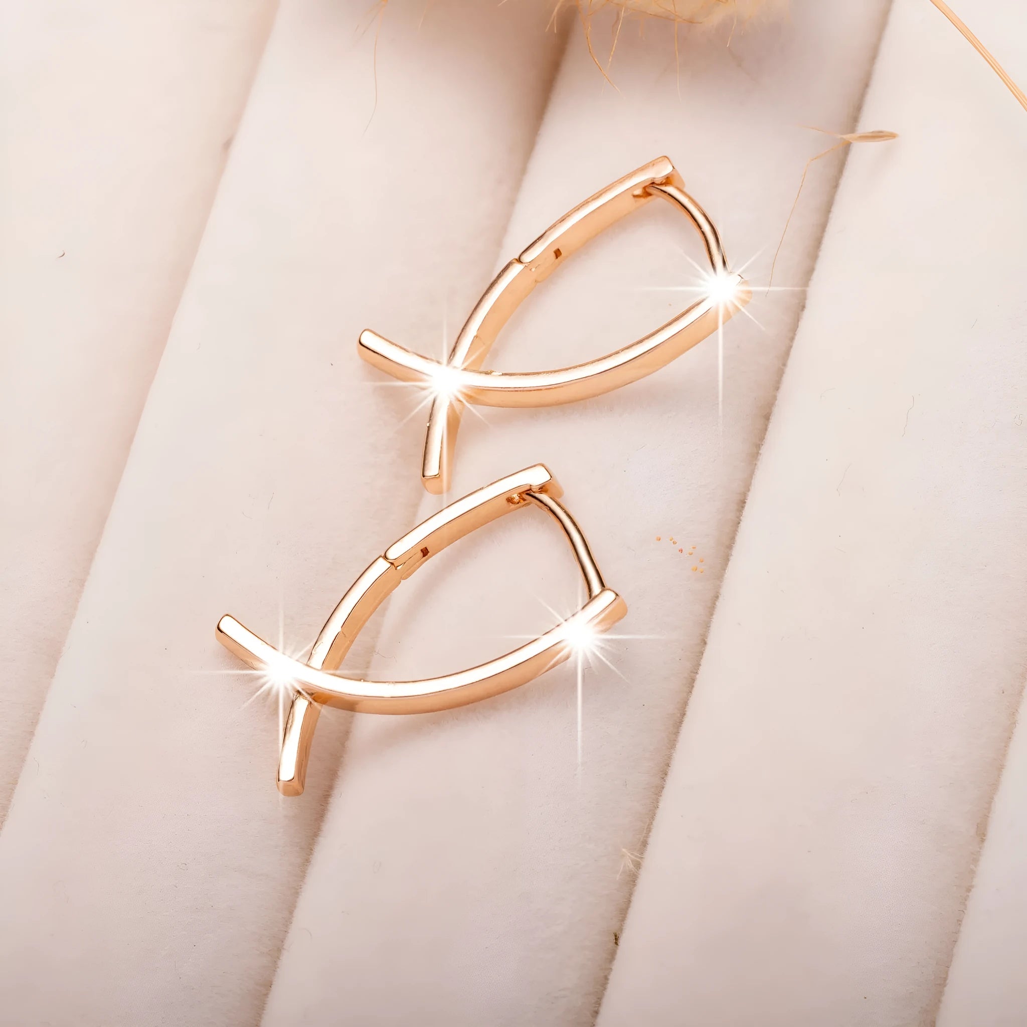 A pair of rose gold finished copper cross shaped drop earrings on a plain background.