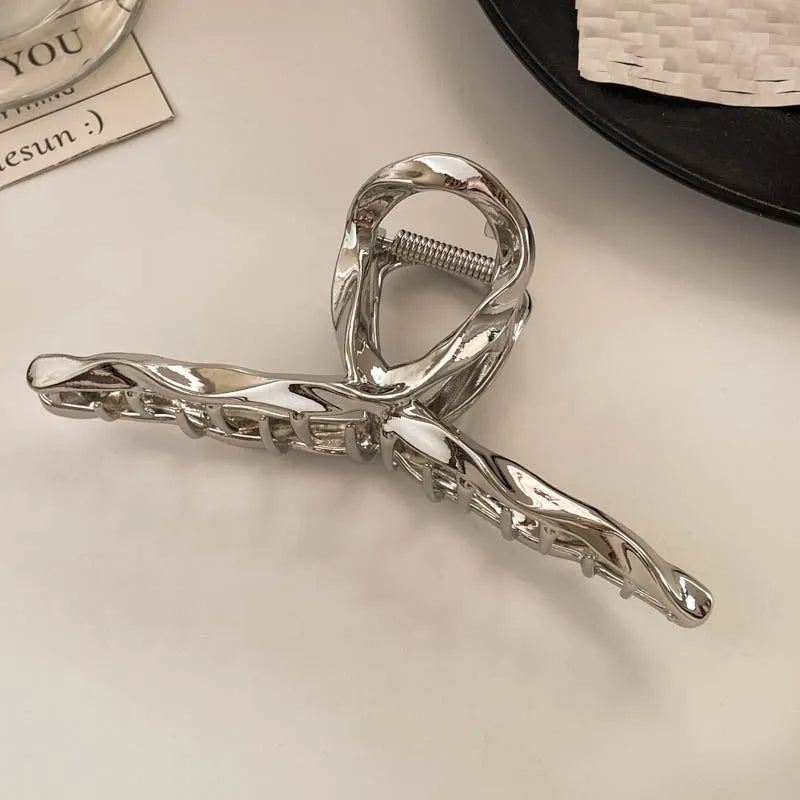Assorted silver metal hair claws and barrettes including wave, knot, bow, and pearl designs on a white background.