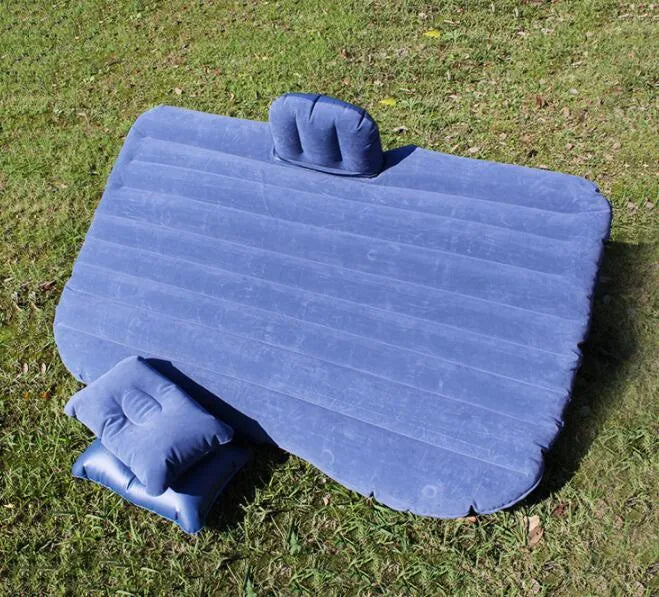 Black inflatable car bed with flocked surface set up in the back of a five-seater vehicle with pillows.