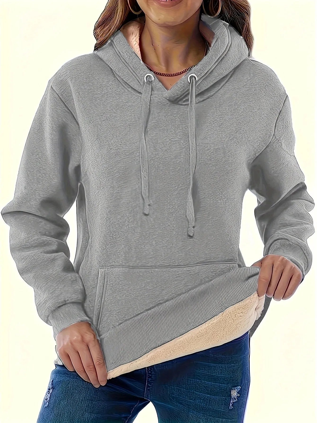 A woman wearing a thick, grey, loose-fit hooded sweatshirt with a 3D pattern and front pockets.