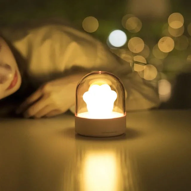 Grey or pink cat paw shaped USB rechargeable night light and music box on a desktop.