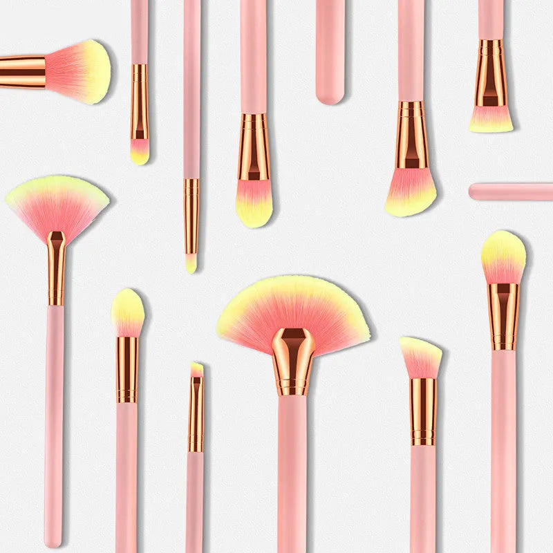 Twelve pink makeup brushes with nylon bristles and wood handles laid out in a row on a light background