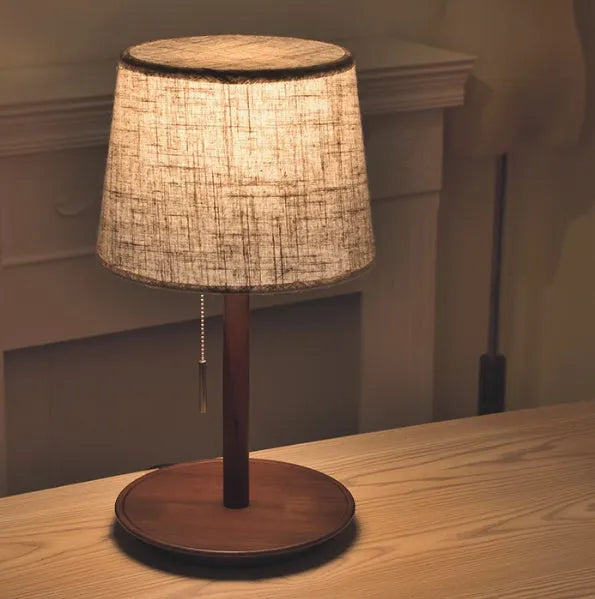 Walnut coloured solid wood bedside table lamp with a white cloth lampshade.