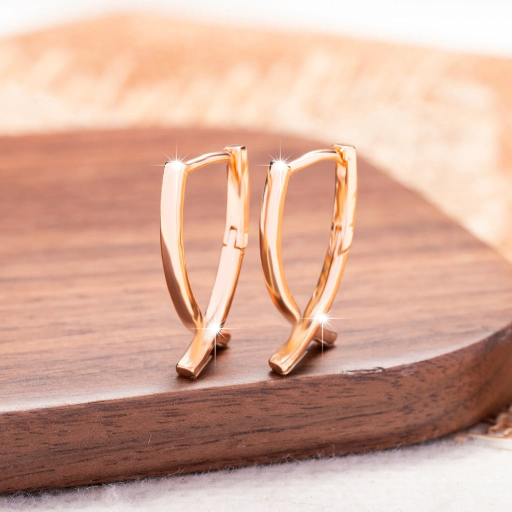 A pair of rose gold finished copper cross shaped drop earrings on a plain background.