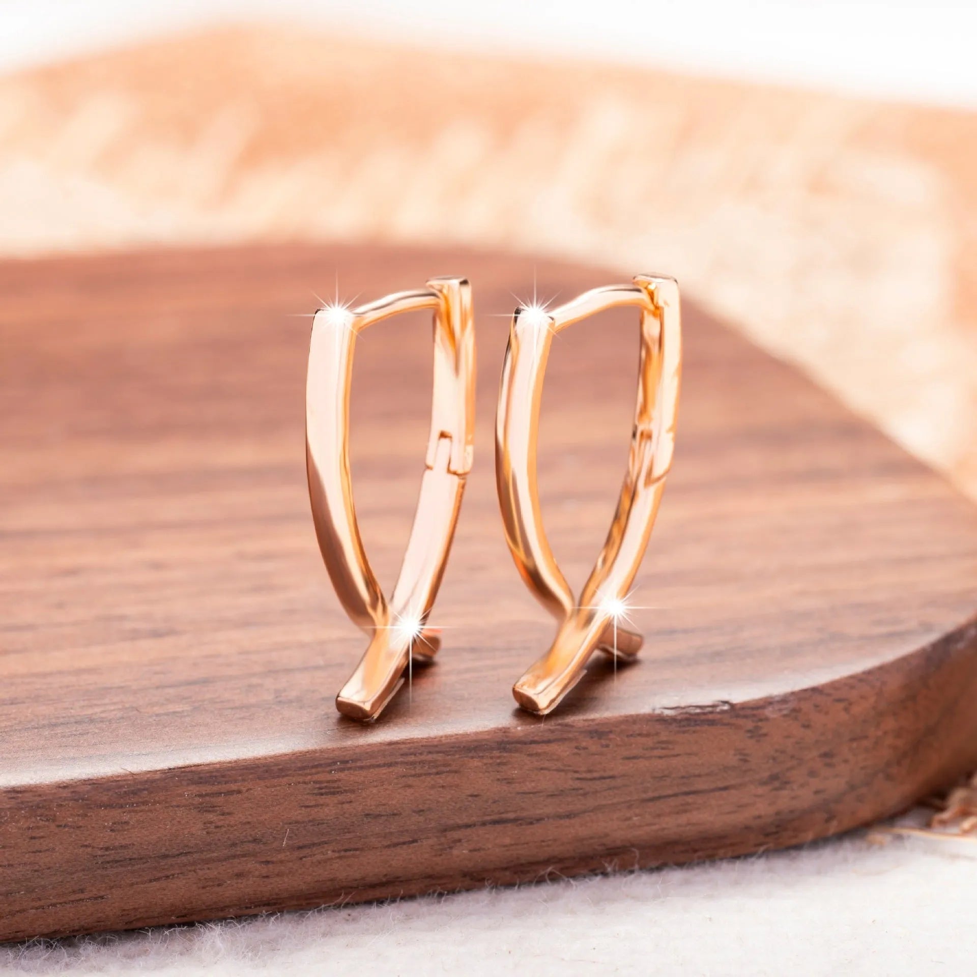 A pair of rose gold finished copper cross shaped drop earrings on a plain background.