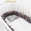 Braided knot crib bumper in spandex velvet, shown bending to fit a white wooden cot.