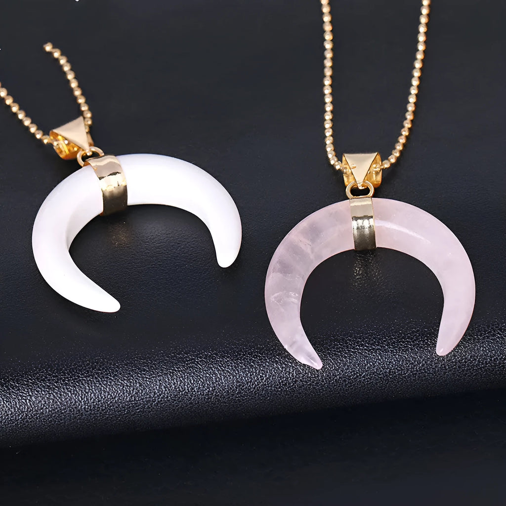 Close-up of a moon pendant necklace with a pink natural stone, on a copper-coloured chain against a neutral background.