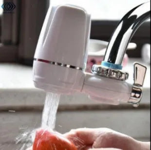 White plastic kitchen tap water filter with ceramic cartridge and universal adapter kit on a counter.