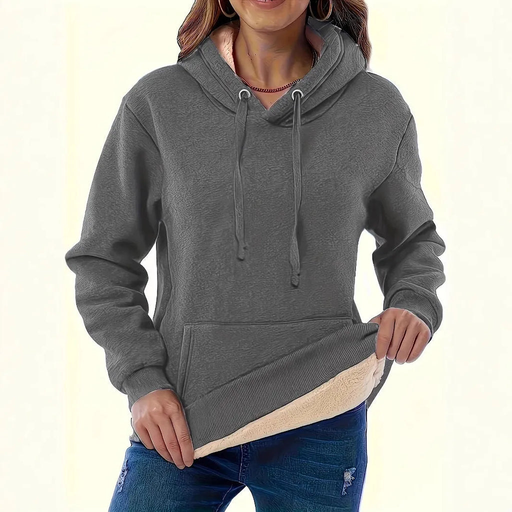 A woman wearing a thick, grey, loose-fit hooded sweatshirt with a 3D pattern and front pockets.