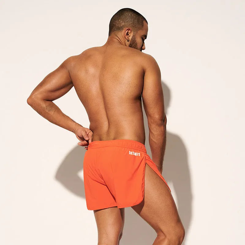Man wearing loose orange red polyester beach shorts with elasticated waistband.