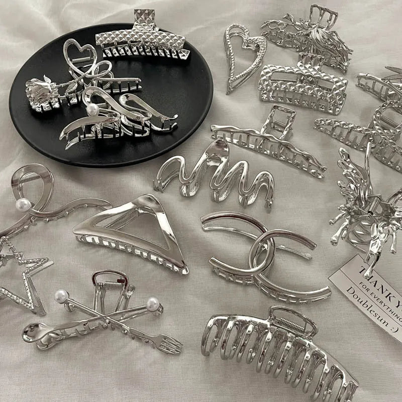 Assorted silver metal hair claws and barrettes including wave, knot, bow, and pearl designs on a white background.
