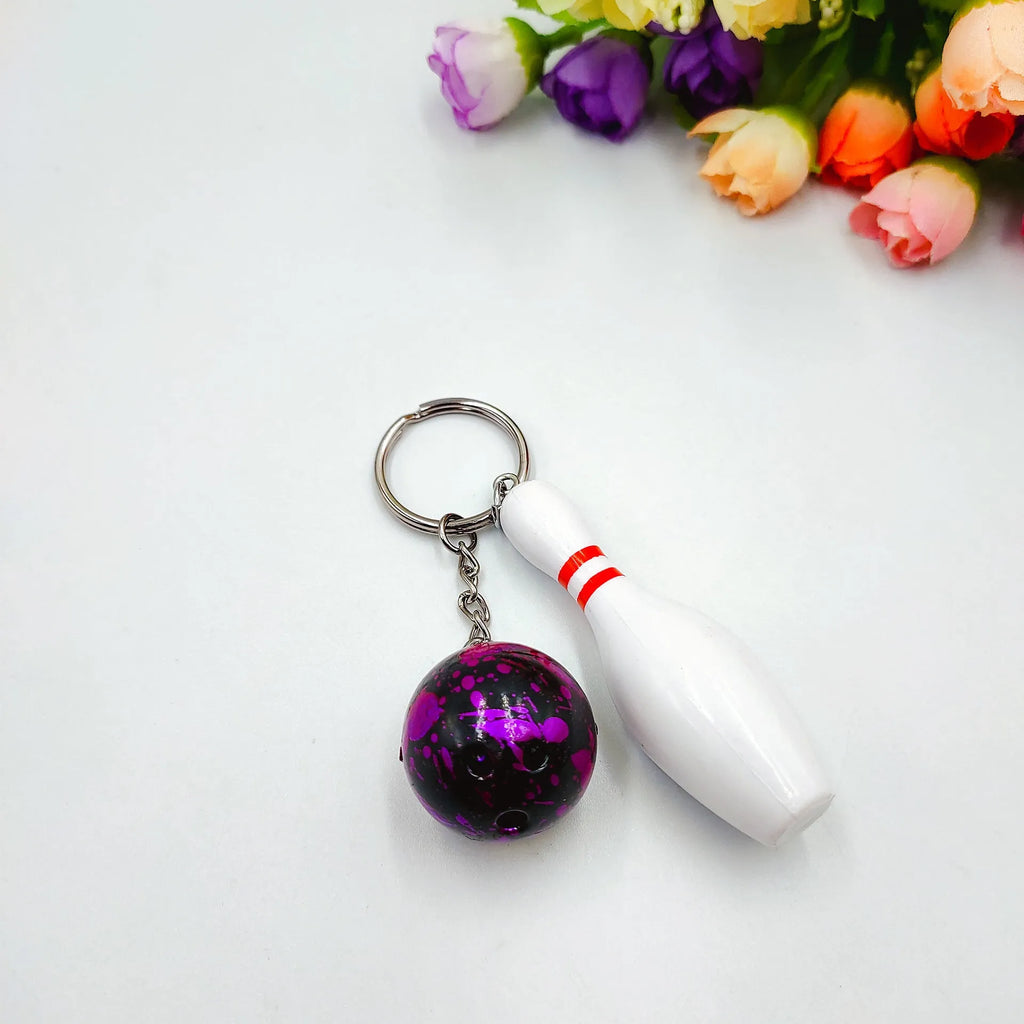 Miniature dark red bowling ball keychain on a metal key ring against a white background.