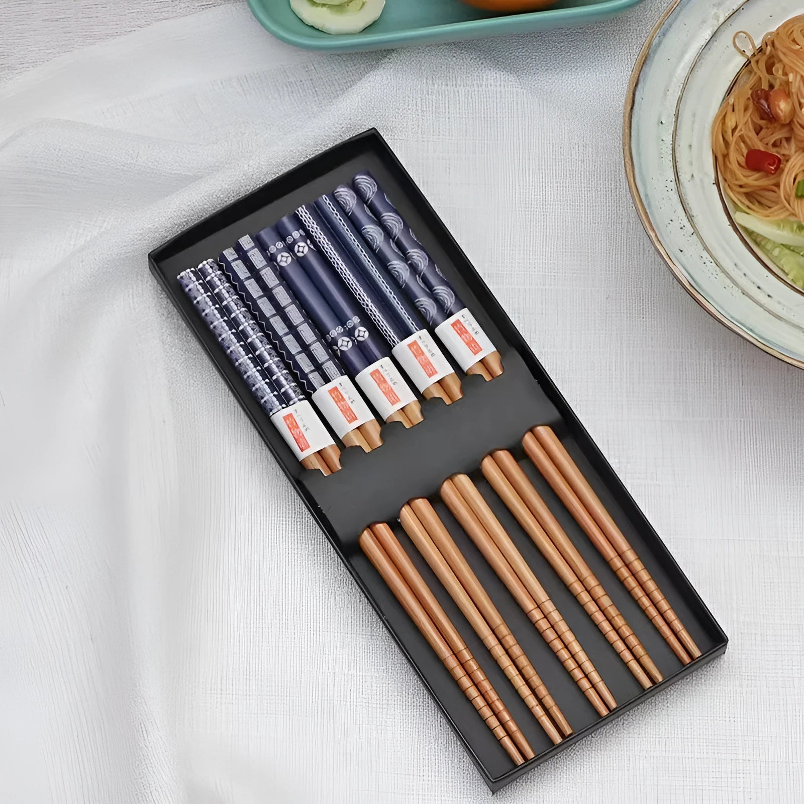 Set of five pairs of bamboo chopsticks with Japanese lucky cat and elegant blue patterns on a table.