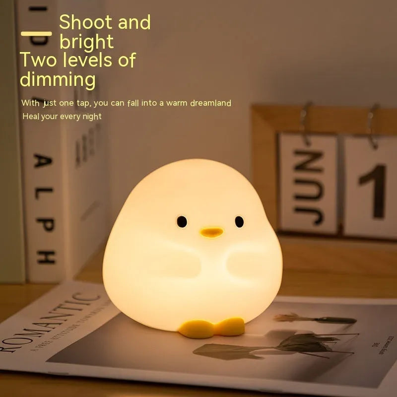 Cute duck-shaped silicone LED night lamp on a bedside table with warm light