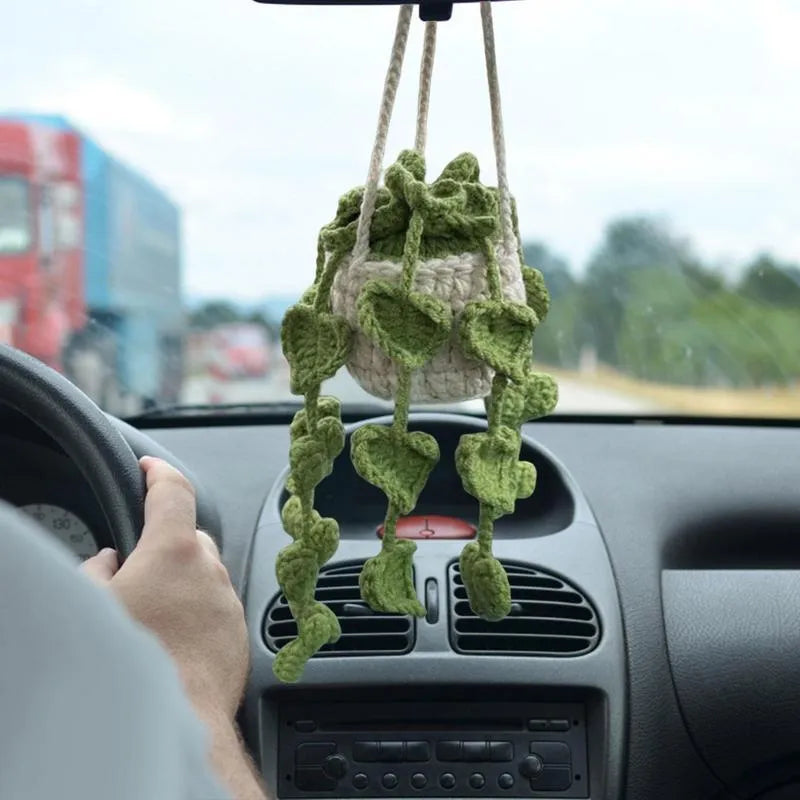 Green and white knitted wool car plant decoration with macramé texture and a white hanging rope.