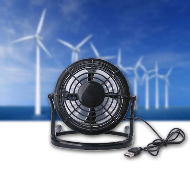 Mini black USB desk fan with adjustable head on a wooden desk next to a laptop.