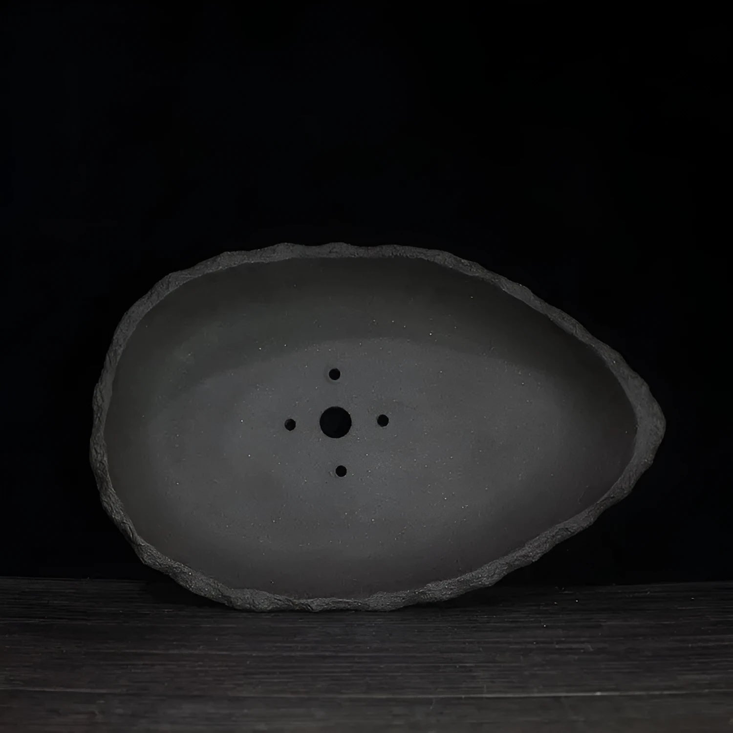 Handmade purple clay flowerpot in a unique shape, shown on floor beside a plant.