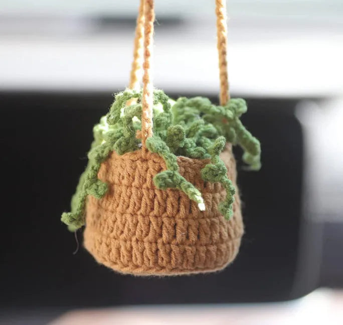 Green and white knitted wool car plant decoration with macramé texture and a white hanging rope.