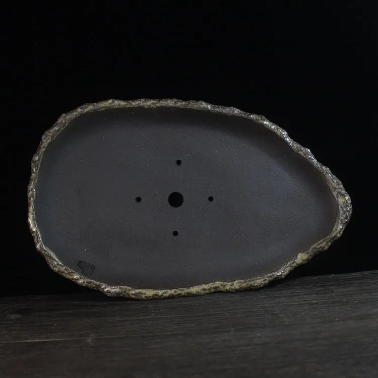 Handmade purple clay flowerpot in a unique shape, shown on floor beside a plant.