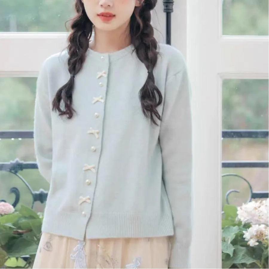 Women's solid colour cardigan with bow and pearl buttons, cashmere acrylic blend, shown in multiple colour options.