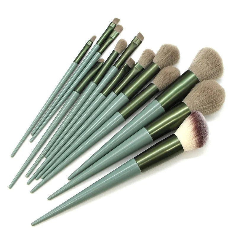 13 green makeup brushes with fibre wool bristles and aluminium tubes arranged on a surface