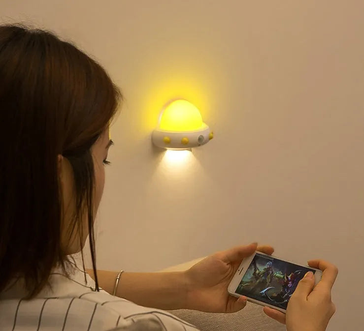 Blue UFO-shaped bedside night light with remote control on a wooden table.