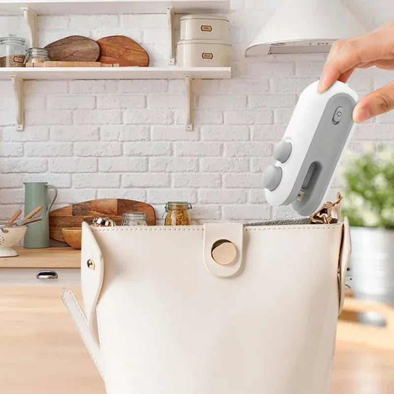 White and blue handheld USB rechargeable heat sealer for sealing food bags with magnetic back.