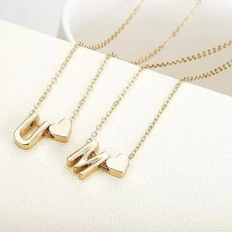 Golden peach heart shaped alloy necklace pendant with a letter design on a white background.