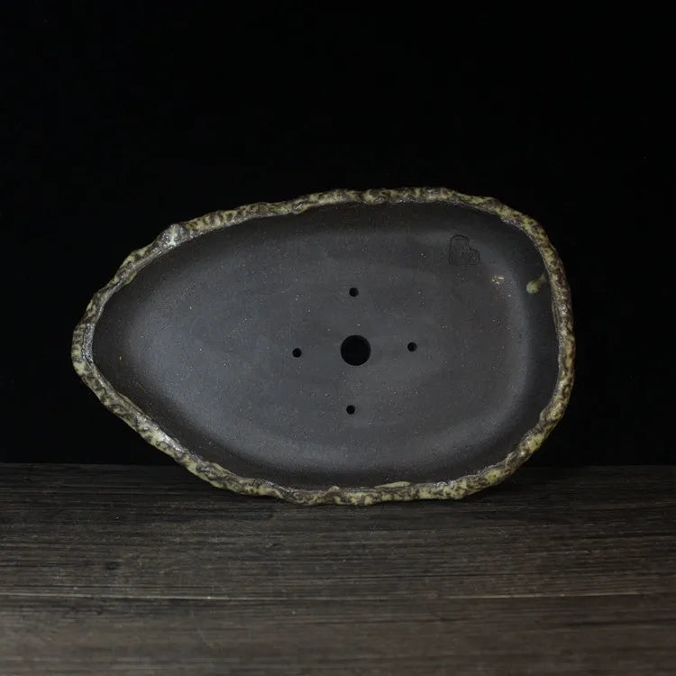 Handmade purple clay flowerpot in a unique shape, shown on floor beside a plant.