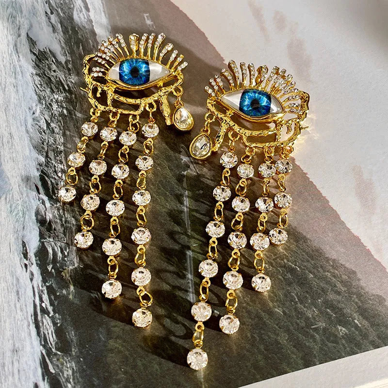 Pair of gold plated long tassel earrings with artificial crystal and zircon elements, eye motif, on white background