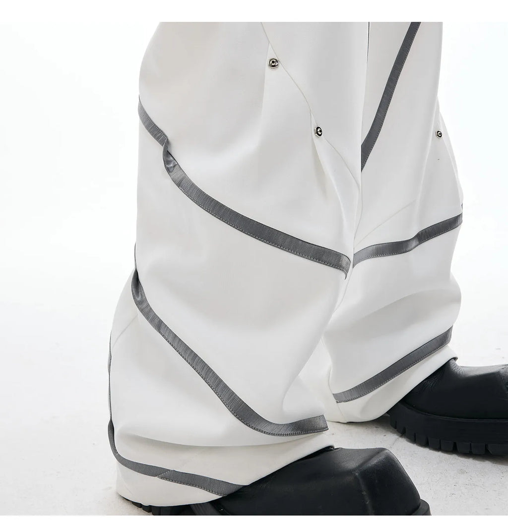 Men's black and white deconstructed trousers with metal striped rivets and front pleats.