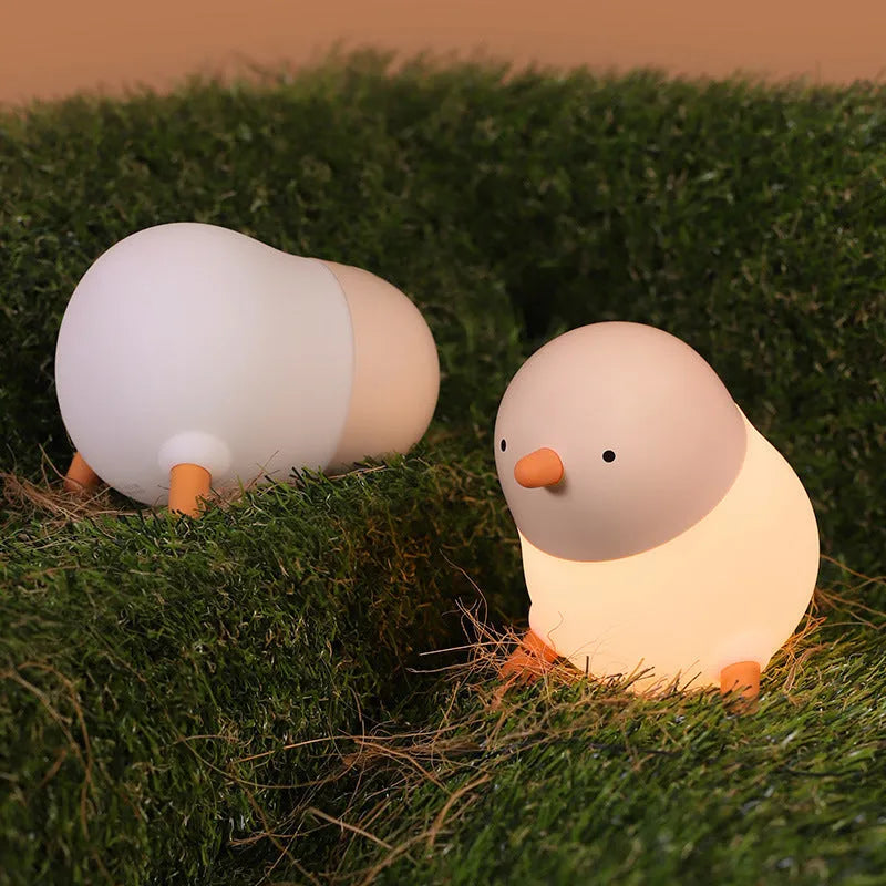 Pecking rice chicken small night light with warm yellow glow on a wooden bedside table, USB charging cable visible