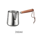 Stainless steel barista milk cup with measurement scale markings and a wooden handle.