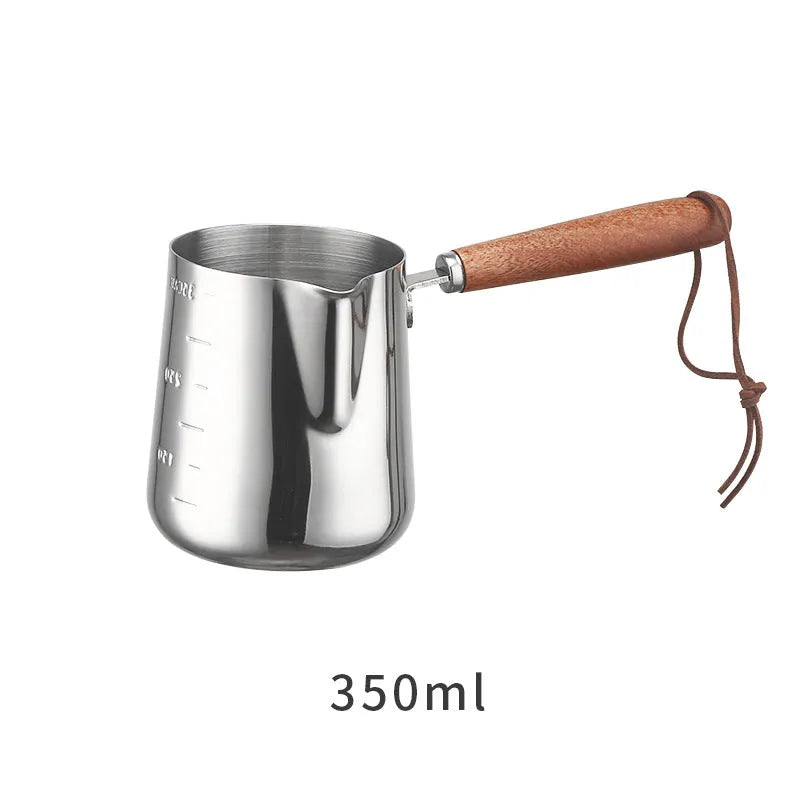 Stainless steel barista milk cup with measurement scale markings and a wooden handle.