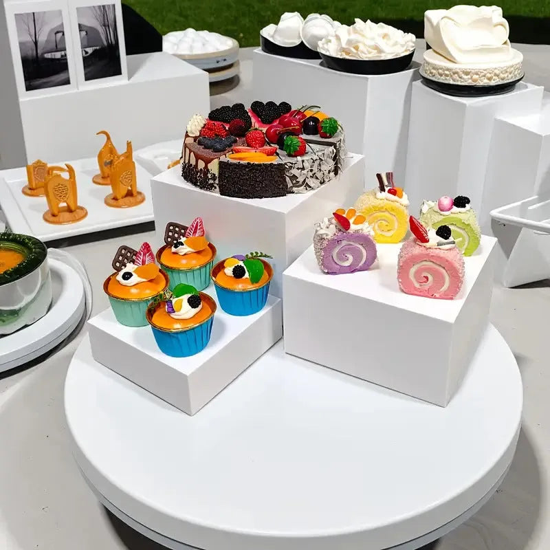 Set of six white geometric cube-shaped plastic dessert display stands arranged on a table.
