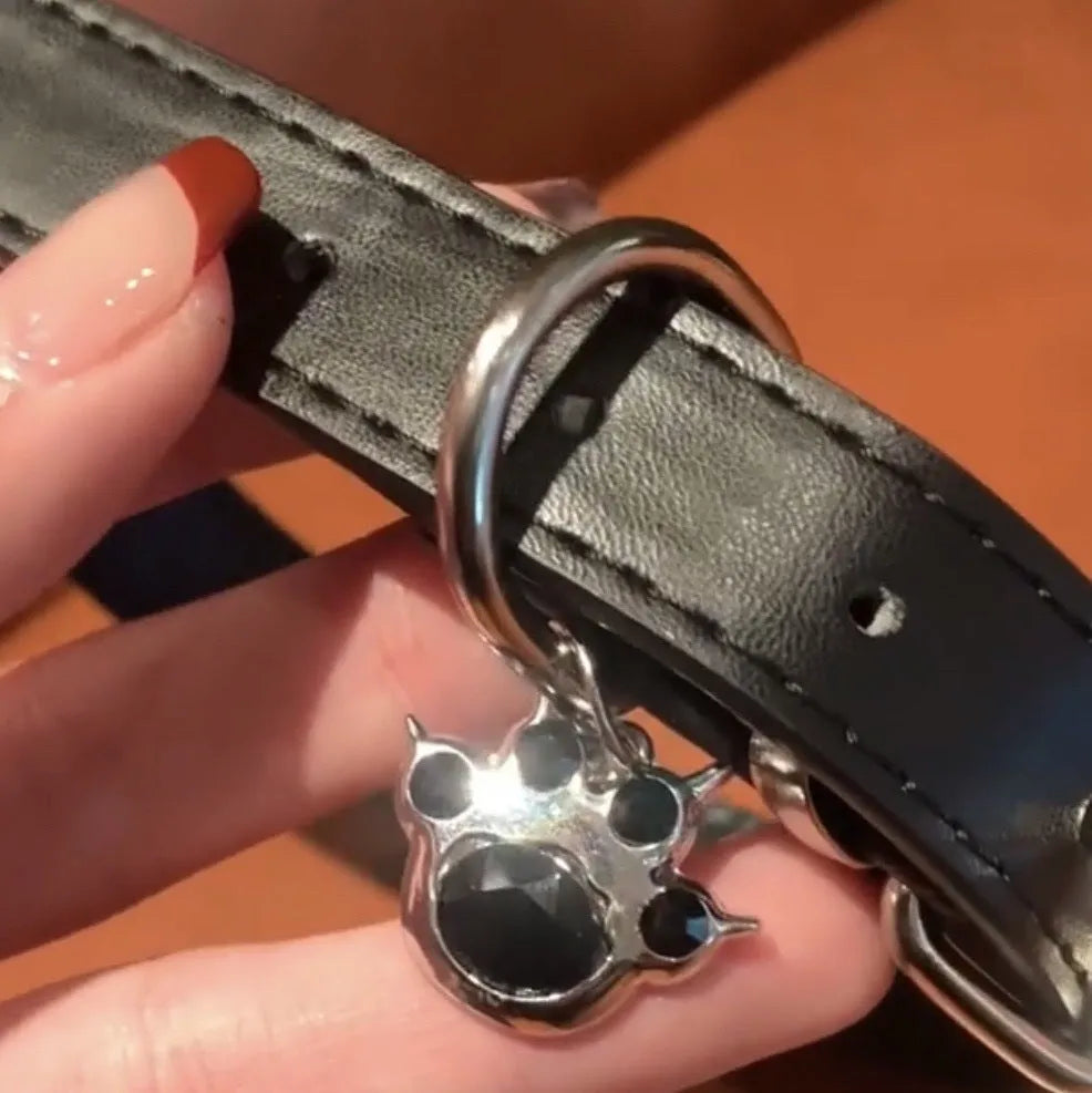 Black leather adjustable dog collar with a small bell charm, shown in cat's paw, bone, and plain design variants.