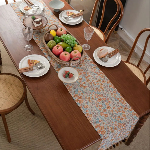 Beige jacquard fabric table runner with long tassels and a woven floral leaf pattern.