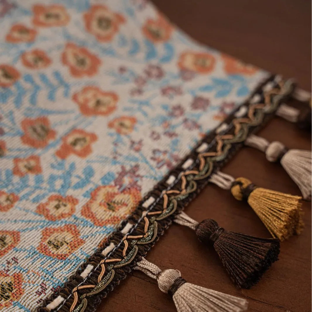 Beige jacquard fabric table runner with long tassels and a woven floral leaf pattern.