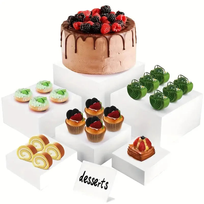 Set of six white geometric cube-shaped plastic dessert display stands arranged on a table.