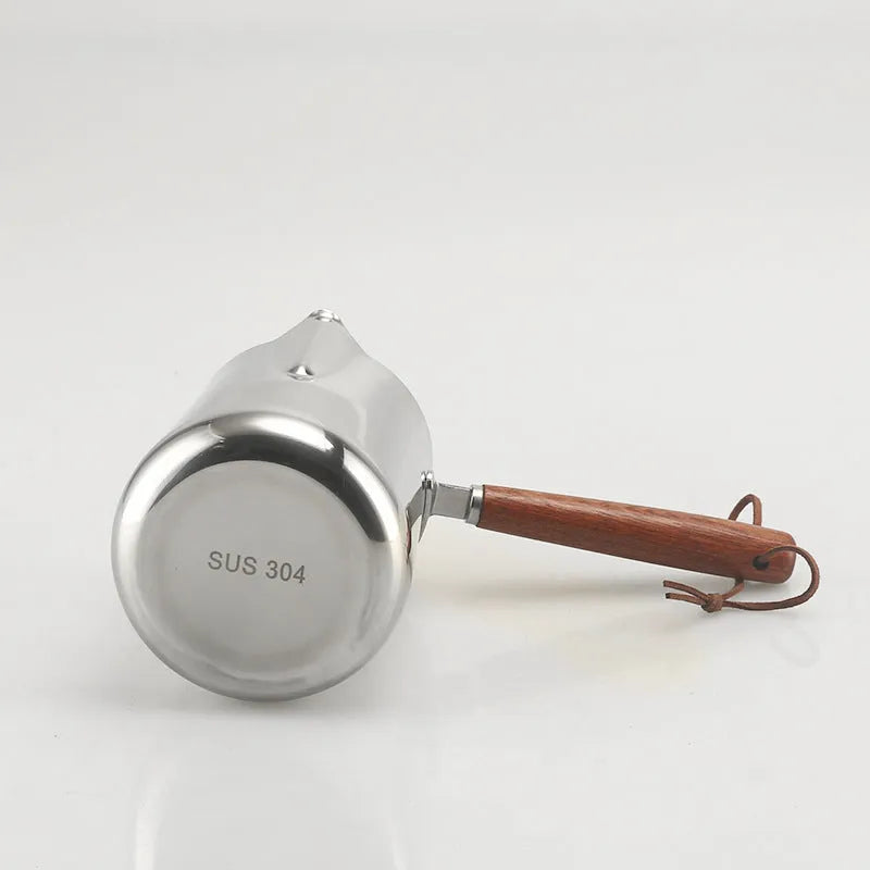 Stainless steel barista milk cup with measurement scale markings and a wooden handle.