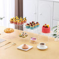Set of six white geometric cube-shaped plastic dessert display stands arranged on a table.