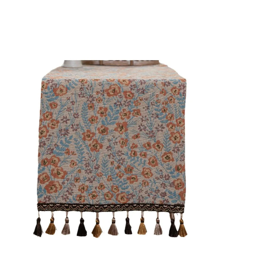Beige jacquard fabric table runner with long tassels and a woven floral leaf pattern.