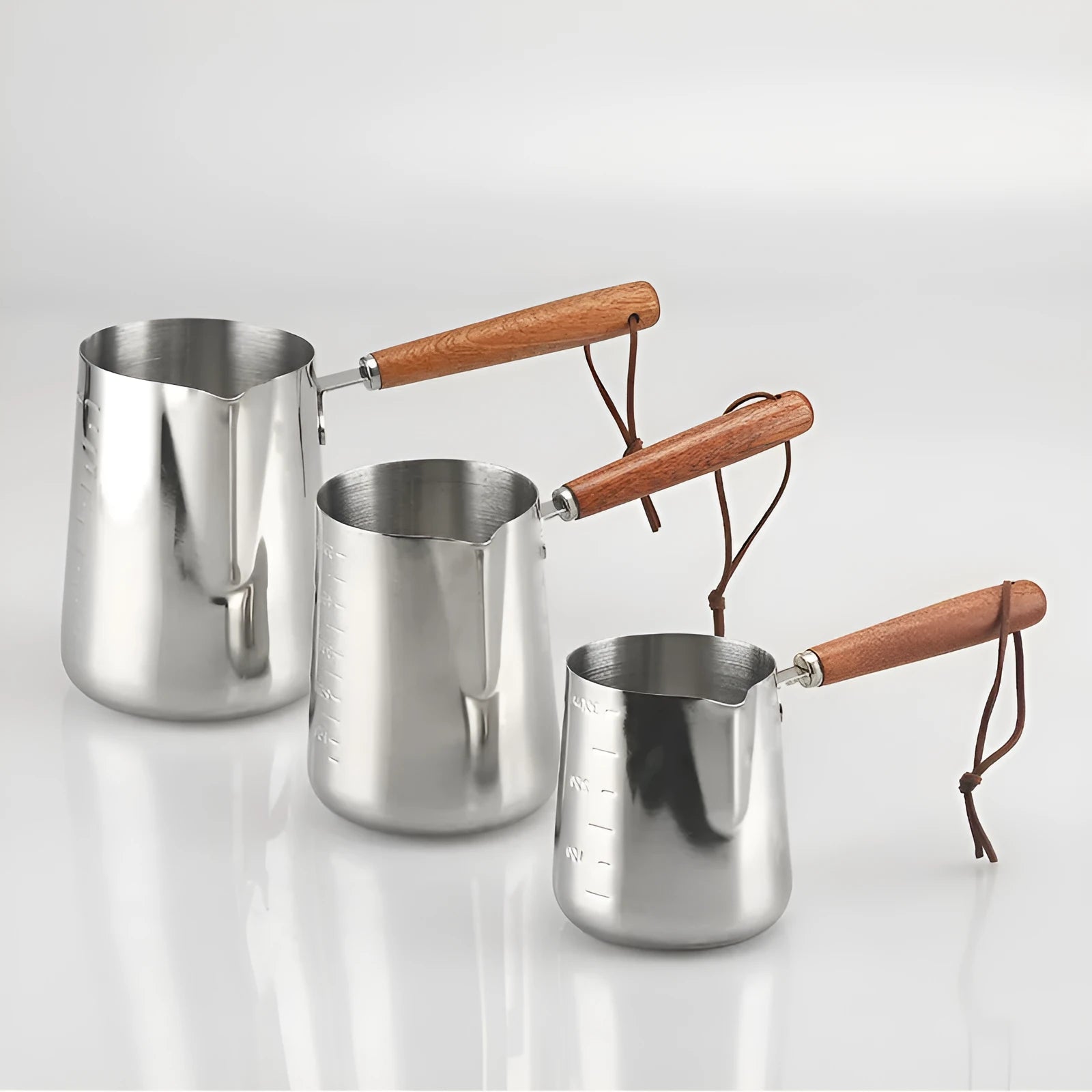 Stainless steel barista milk cup with measurement scale markings and a wooden handle.