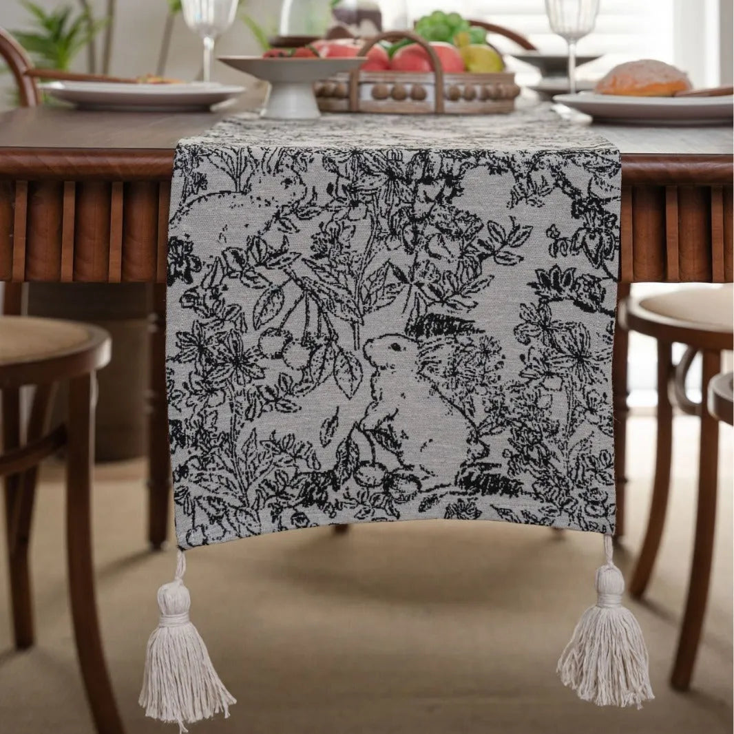 Beige jacquard fabric table runner with long tassels and a woven floral leaf pattern.