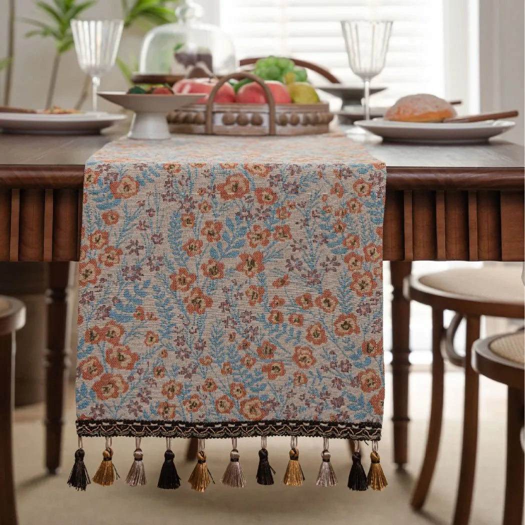 Beige jacquard fabric table runner with long tassels and a woven floral leaf pattern.