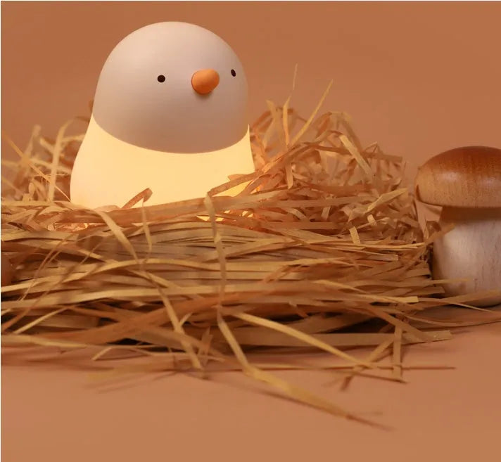 Pecking rice chicken small night light with warm yellow glow on a wooden bedside table, USB charging cable visible